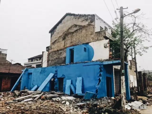 △ 這棟建筑是臨江最近的半拆遷建筑物的遺留，沅江和堤壩成為了展覽的天然背景。創(chuàng)作團(tuán)隊(duì)對(duì)這棟建筑進(jìn)行了半涂裝，將符號(hào)性的沅水曲線與拆遷進(jìn)行中的建筑立面進(jìn)行意義的疊造，它們共同觸發(fā)了場(chǎng)所空間多元語境的生成，把拆遷這種暫時(shí)破壞性、干擾性的介入行動(dòng)與沅水右岸發(fā)展的未來性、美好性緊密融合。